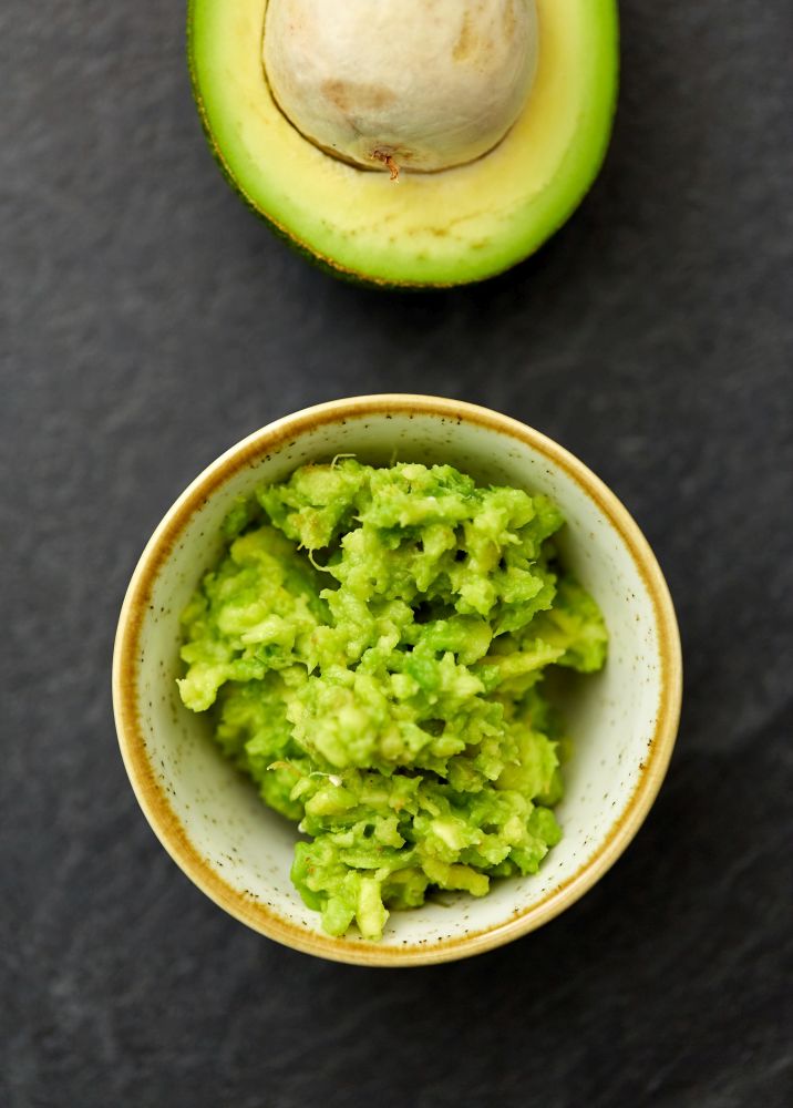 food, eating and vegetable concept - close up of mashed avocado in ceramic bowl on slate stone background. close up of mashed avocado in ceramic bowl