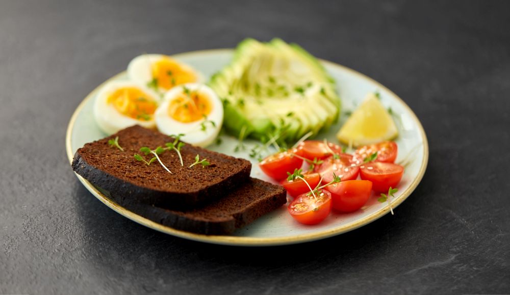 food, eating and breakfast concept - toast bread with cherry tomatoes, avocado, eggs and greens on ceramic plate. toast bread with cherry tomato, avocado and eggs
