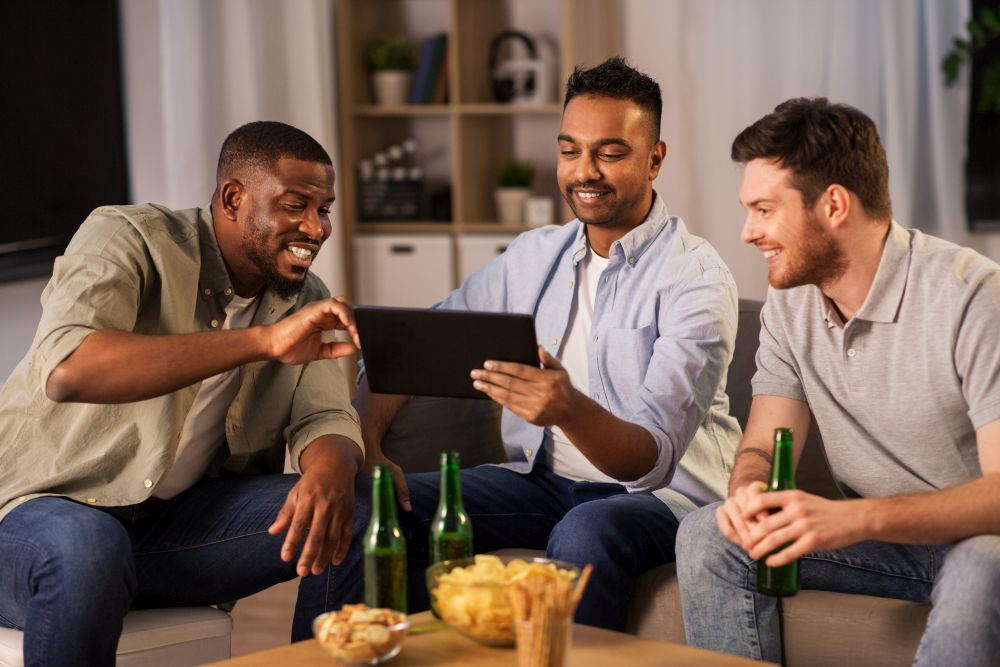 friendship, leisure and people concept - male friends with tablet pc computer drinking beer at home at night. male friends with tablet pc drinking beer at home
