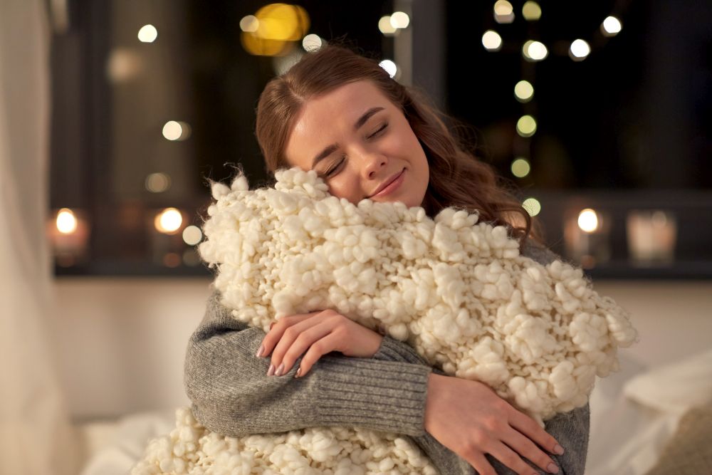 christmas, holiday and people concept - happy young woman with soft pillow in bed at home bedroom at night. happy young woman with soft pillow in bed at home