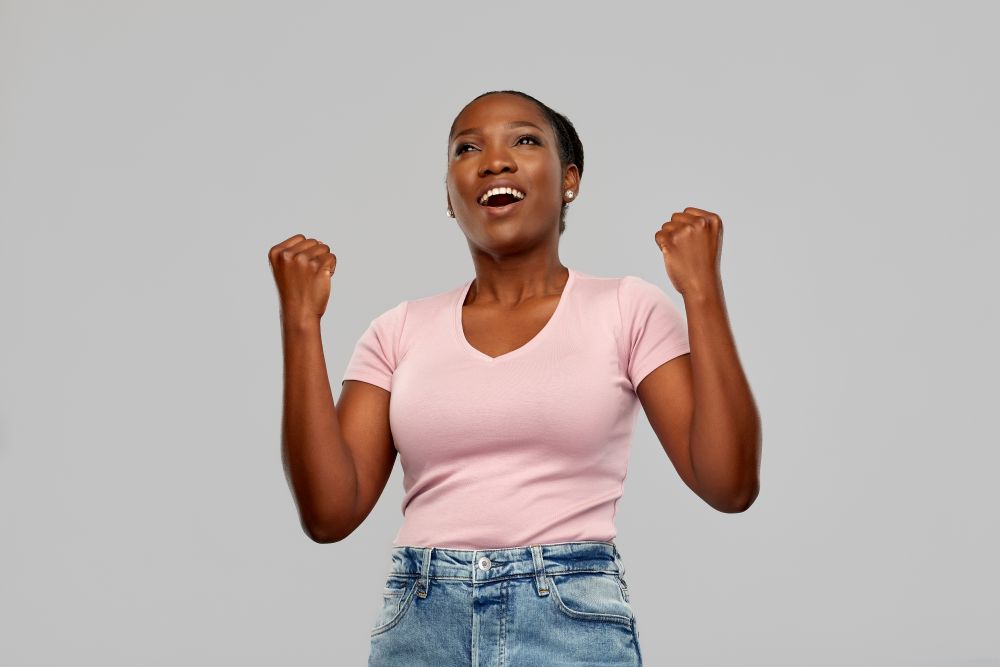 success, winning gesture and people concept - happy smiling young african american woman celebrating victory over grey background. happy african american woman celebrating success