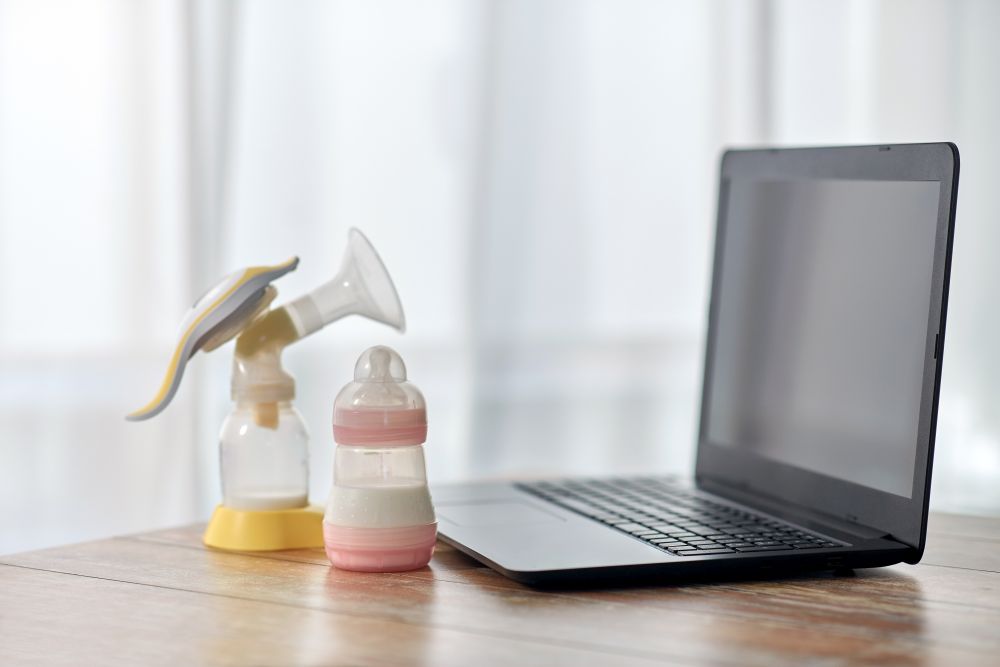 feeding and technology concept - bottle with baby milk formula, breast pump and laptop computer on wooden table at home. baby milk formula, breast pump and laptop