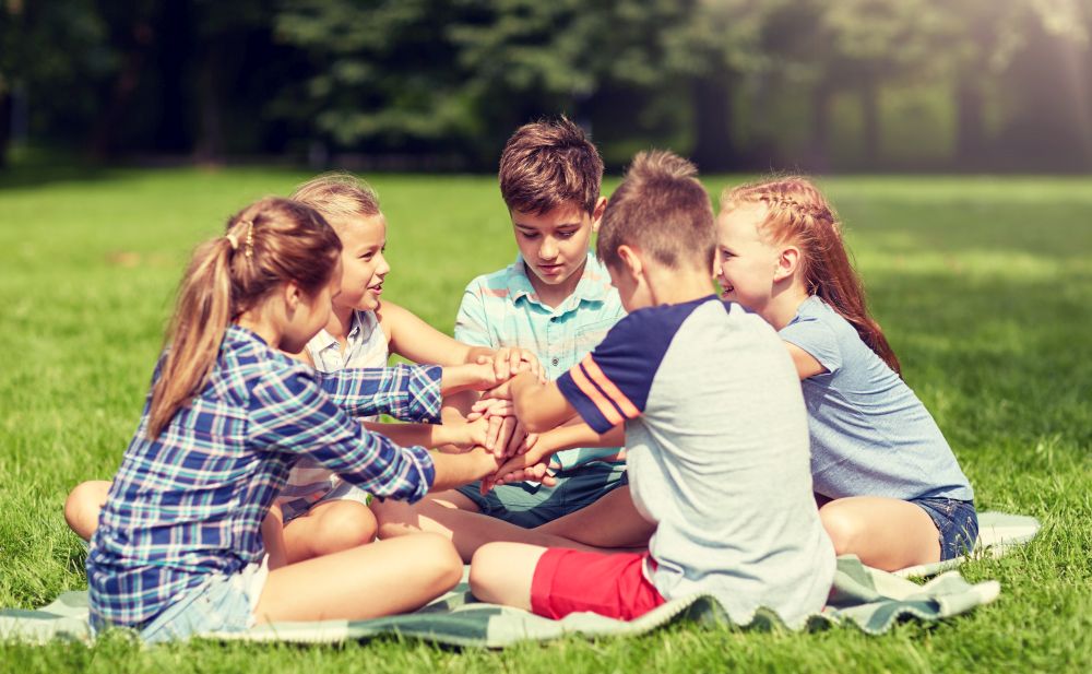 summer holidays, friendship, childhood, leisure and people concept - group of happy pre-teen kids putting hands together in park. group of happy kids putting hands together