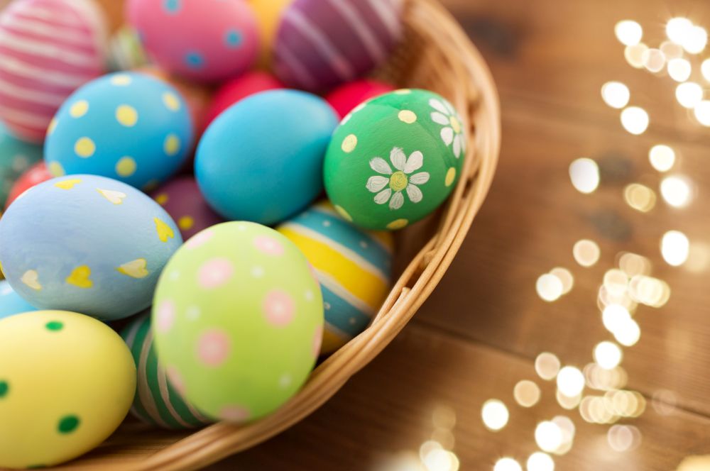 easter, holidays and tradition concept - close up of colored eggs in basket on wooden table. close up of colored easter eggs in basket