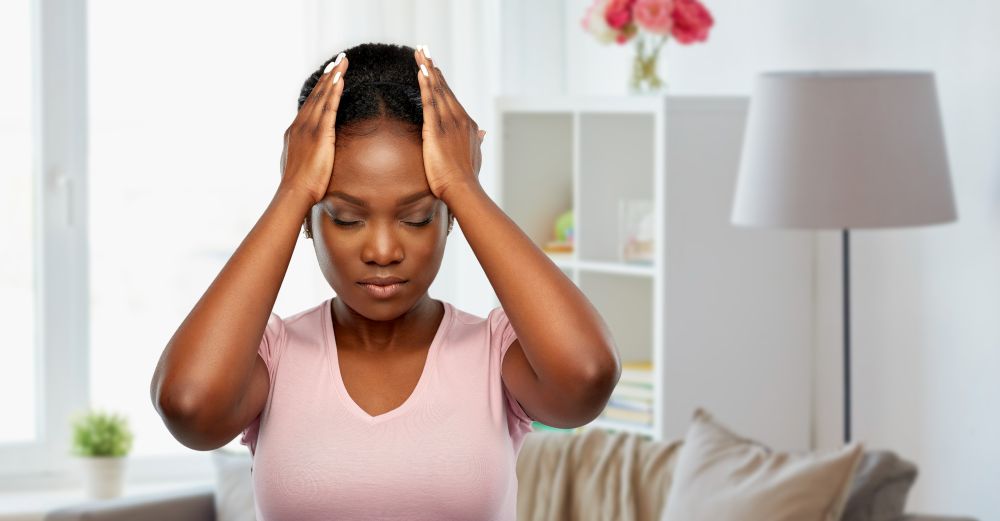 people, health problem and stress concept - unhappy african american woman suffering from headache over home room background. african american woman suffering from headache