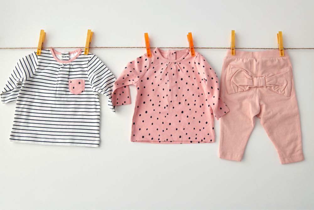 clothes, laundry, babyhood and clothing concept - set of shirts and pants for baby girl with prints hanging on clothesline with pins on white background. shirts and pants for baby girl on clothesline