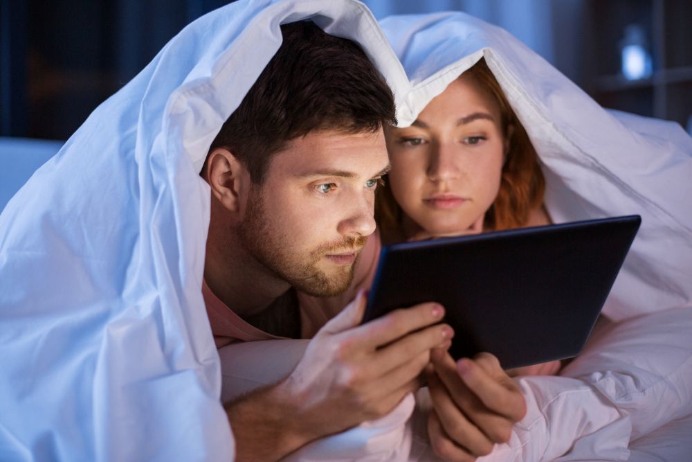technology, internet and people concept - couple using tablet pc computer in bed at night. couple using tablet pc in bed at night