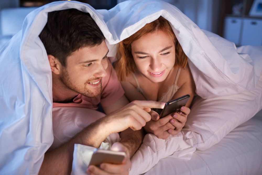 technology, internet and people concept - happy couple using smartphones in bed at night. happy couple using smartphones in bed at night
