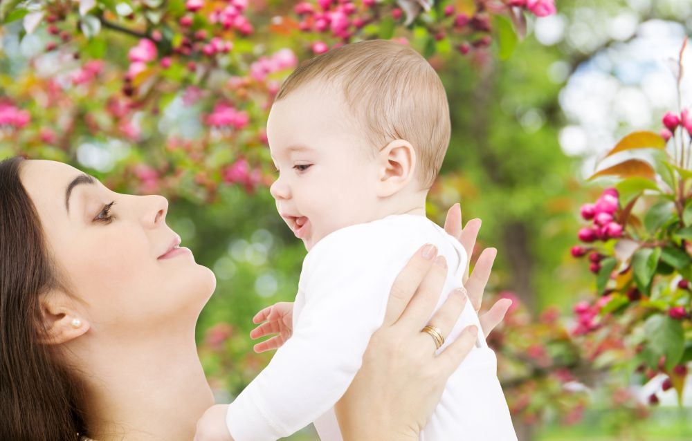 family and motherhood concept - happy smiling young mother with little baby over natural spring cherry blossom background. mother with baby over spring garden background