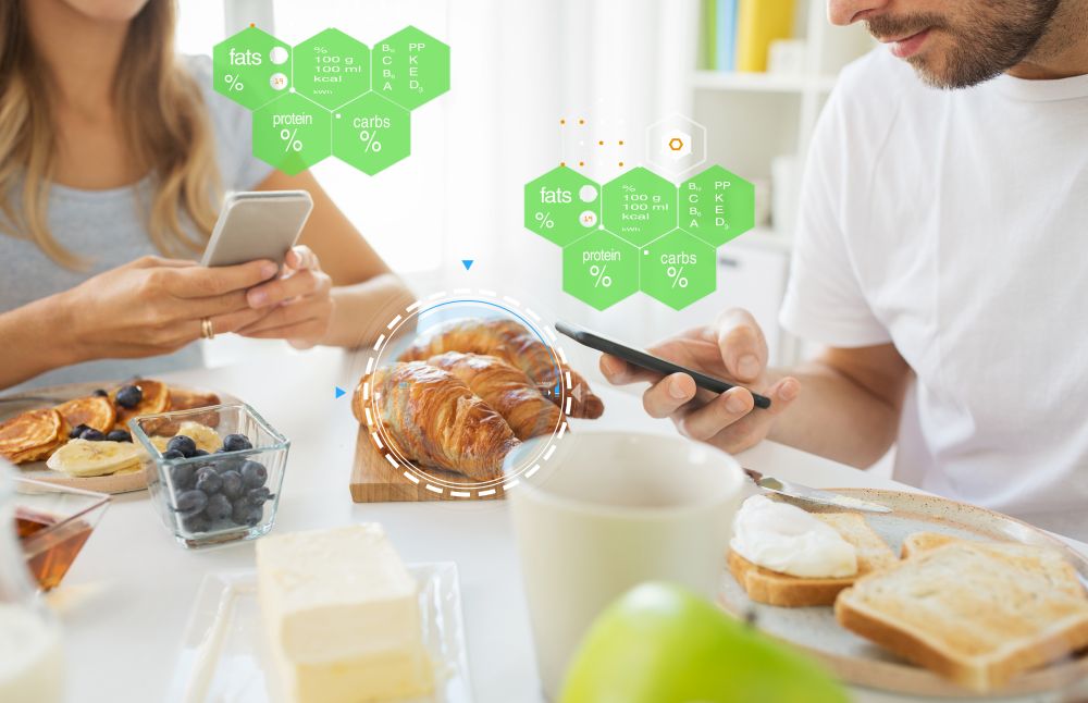 eating, people and technology concept - close up of couple with smartphones having breakfast at home over food nutritional value chart. couple with smartphones having breakfast at home