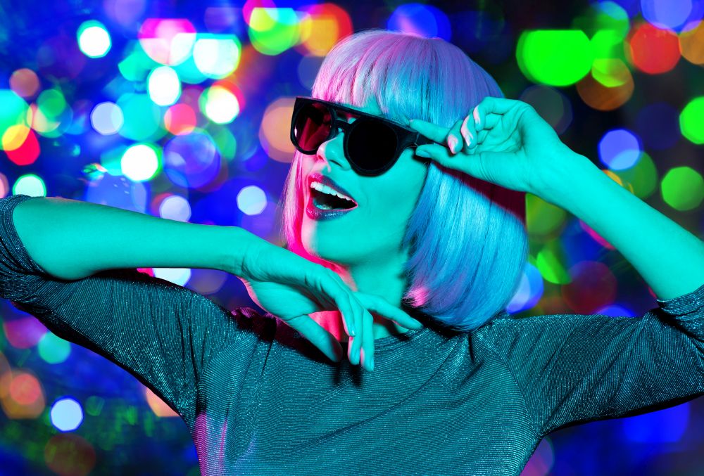 nightlife, fashion and people concept - happy young woman wearing pink wig and black sunglasses dancing over night lights background. happy woman in pink wig and sunglasses dancing