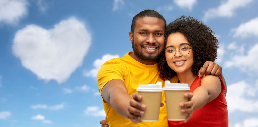 valentines day, love and people concept - happy smiling african american couple with takeaway coffee cups over grey background. happy african american couple with coffee cups