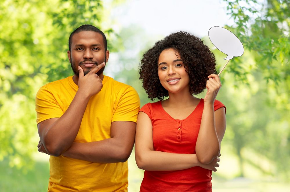 relationships and people concept - happy smiling african american couple with little blank speech bubble over green natural background. african american couple with blank speech bubble