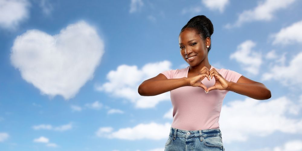 love and valentine&rsquo;s day concept - happy smiling african american young woman making hand heart gesture over grey background. african american woman making hand heart gesture