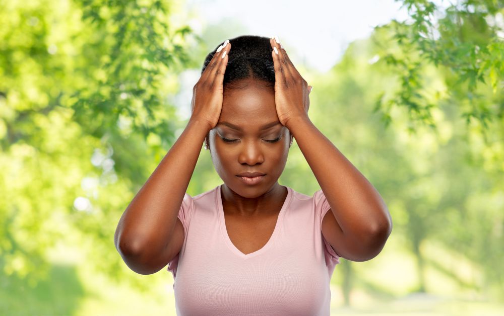 people, health problem and stress concept - unhappy african american woman suffering from headache over green natural background. african american woman suffering from headache