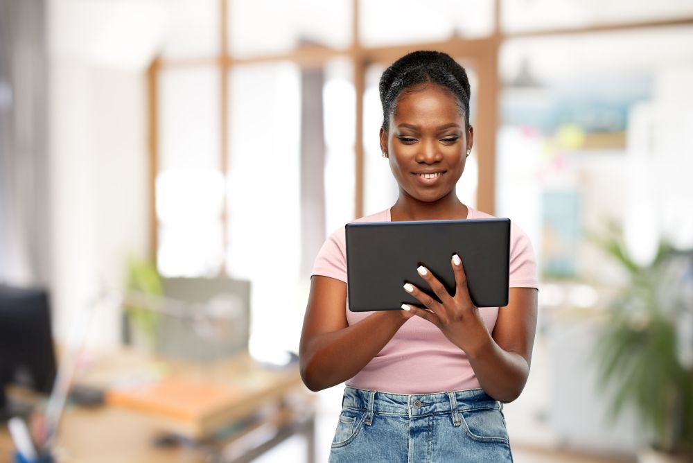 technology, corporate and people concept - happy african american woman using tablet computer over office background. african american woman with tablet pc at office