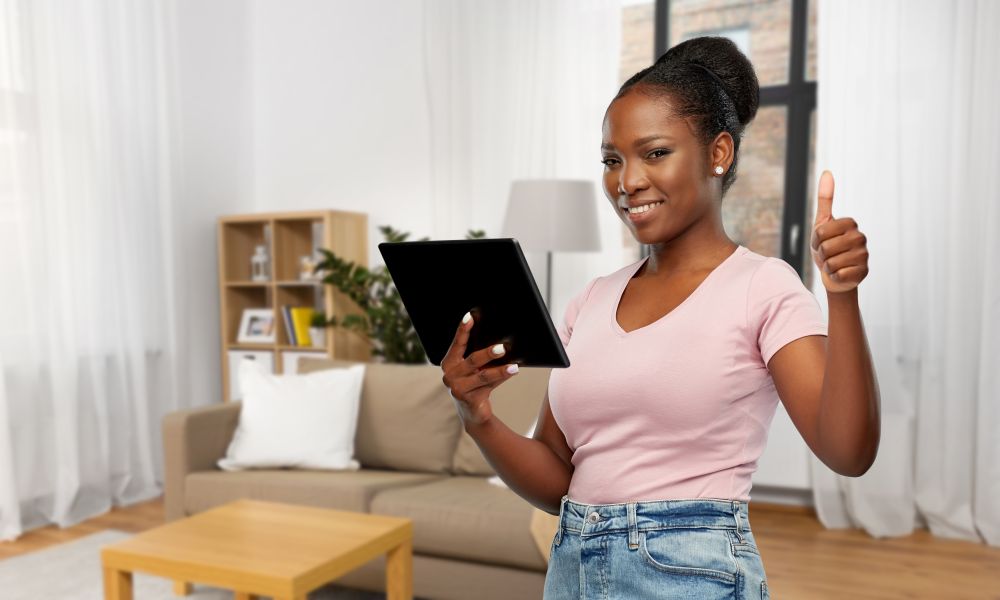 technology, gesture and people concept - happy african american woman with tablet computer showing thumbs up over home room background. african american woman showing thumbs up at home