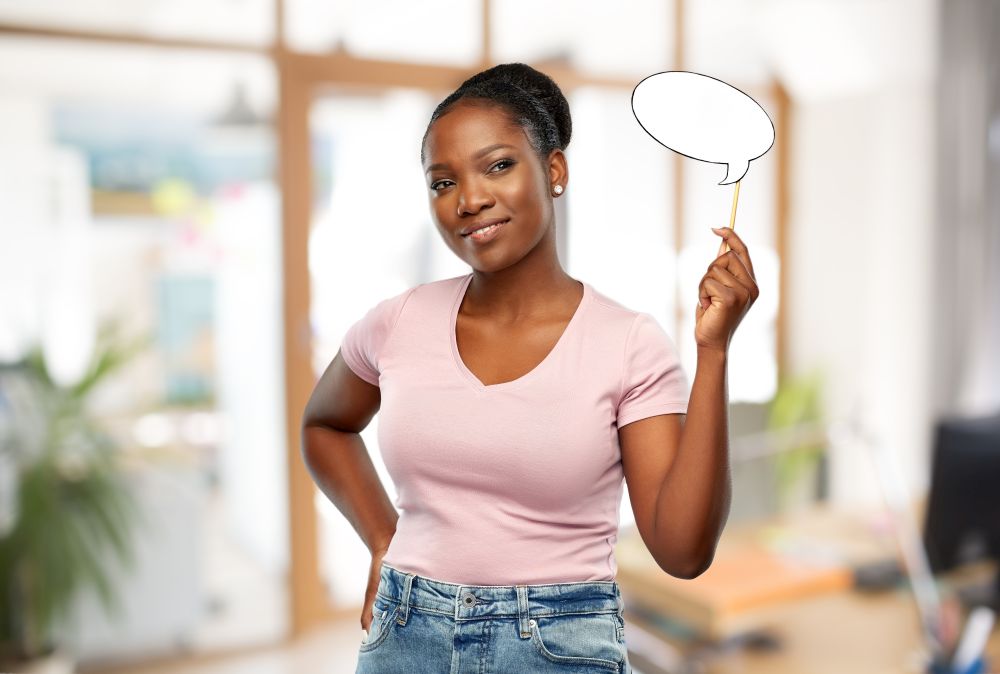 party props, photo booth and communication concept - happy african american young woman holding blank speech bubble over office background. african woman with speech bubble at office