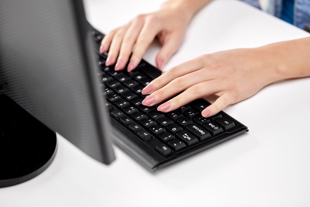 technology and people concept - female hands with red manicure typing on computer keyboard on table. female hands typing on computer keyboard