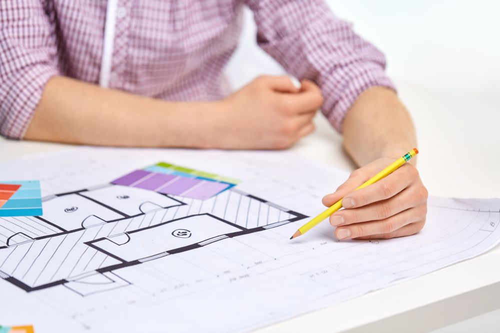interior design, architecture and people concept - close up of architect&rsquo;s hands working with blueprint, pencil and color palettes. architect with blueprint and color palettes