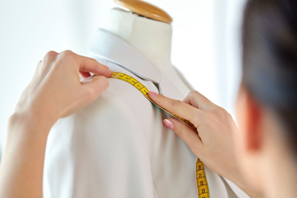 tailoring, sewing and clothing concept - close up of fashion designer measures jacket with tape measure. fashion designer measures jacket with tape measure