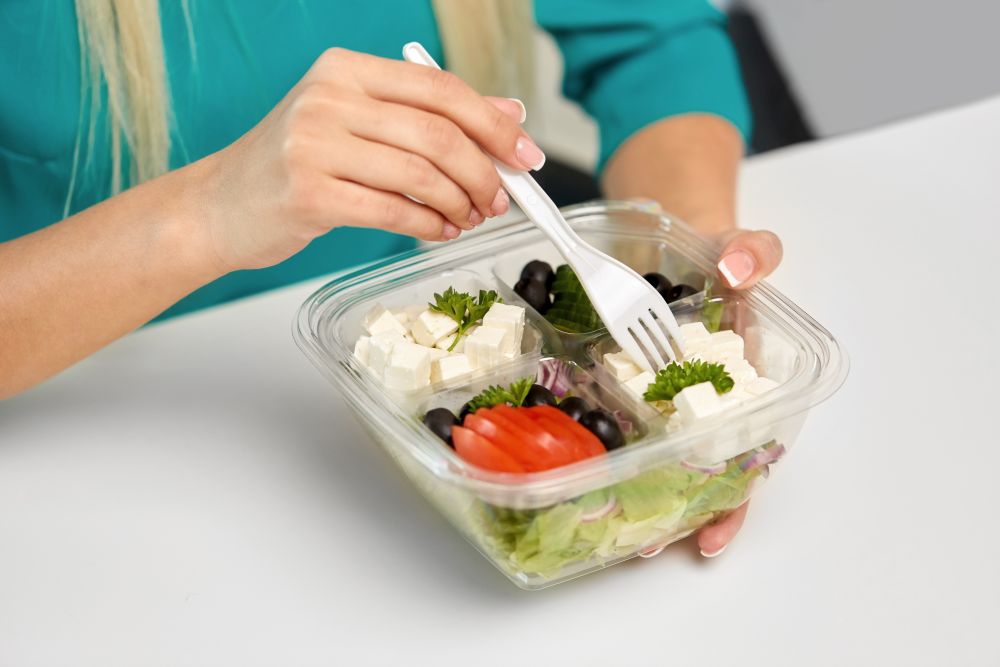 lunch and people concept - hands of woman eating take out food from plastic container. hands of woman eating take out food from container