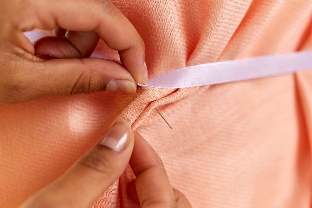 dressmaking and tailoring concept - close up of fashion designer&rsquo;s hands attaching ribbon to cloth with sewing pin. hands attaching ribbon to cloth with sewing pin