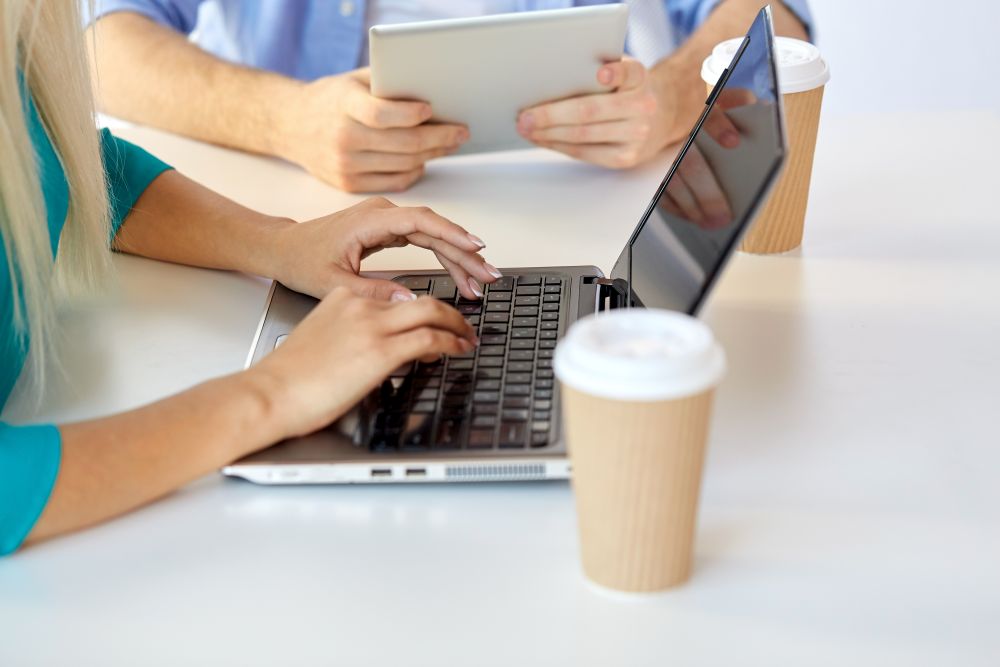 business, break and people concept - close up of woman typing on laptop and coffee cups on table. woman typing on laptop and coffee cups on table