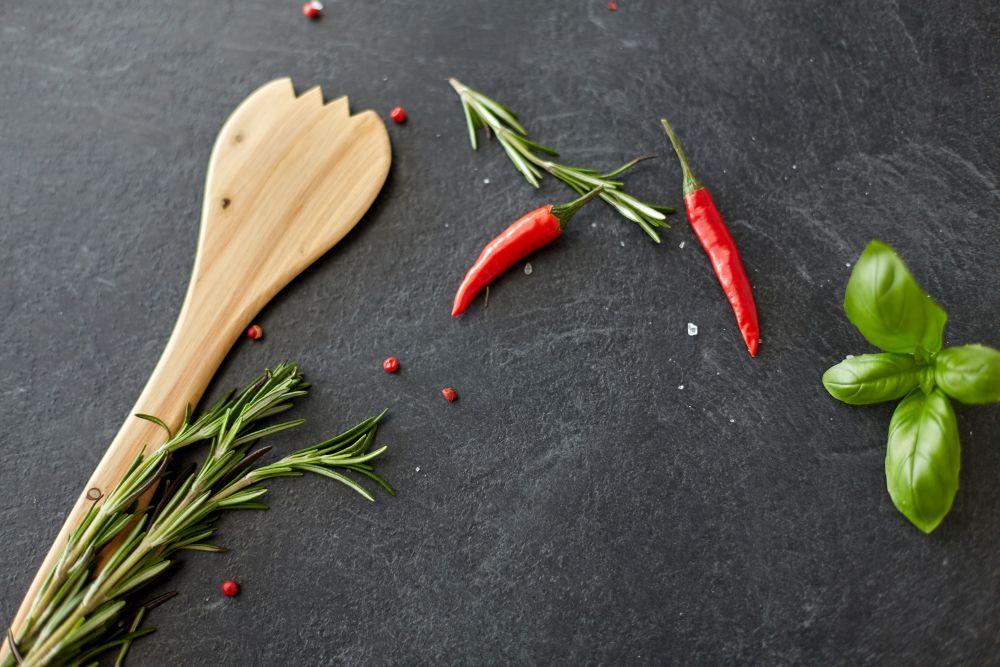 food, culinary and eating concept - rosemary, basil, wooden spatula and red chili pepper on stone surface. rosemary, basil and chili pepper on stone surface