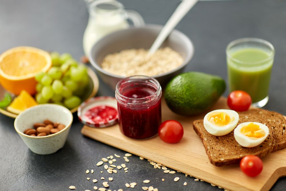 food, eating and breakfast concept - jar with raspberry jam, toast bread, eggs and cherry tomatoes on wooden cutting board. jam, toast bread, eggs, avocado, cherry tomatoes