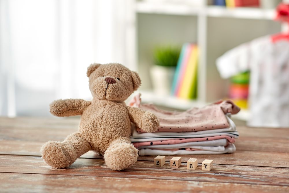 babyhood and clothing concept - baby clothes, teddy bear and toy blocks on wooden table at home. baby clothes and teddy bear toy on table at home