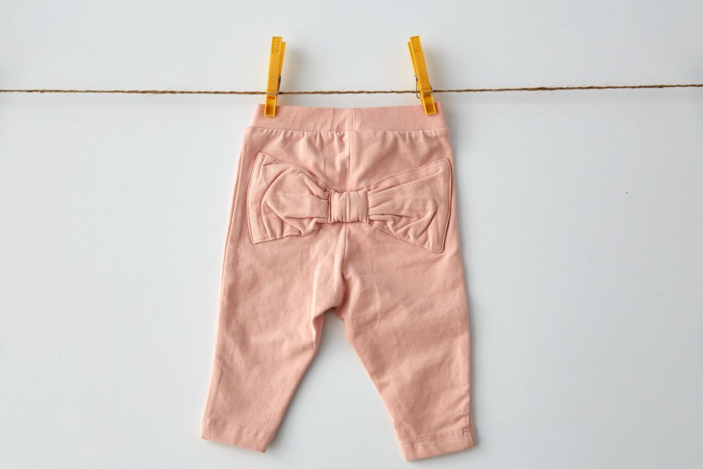 clothes, laundry, babyhood and clothing concept - pink pants for baby girl with bow hanging on clothesline with pins on white background. pink pants for baby girl on clothesline with pins