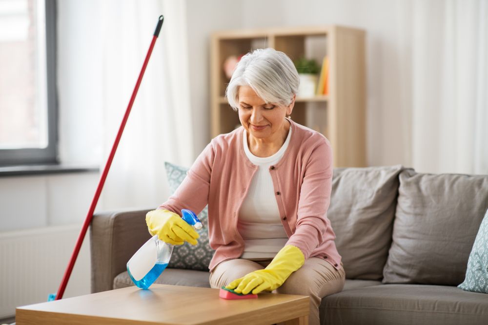 household and people concept - happy senior woman with detergent and sponge cleaning table at home. senior woman with detergent cleaning table at home
