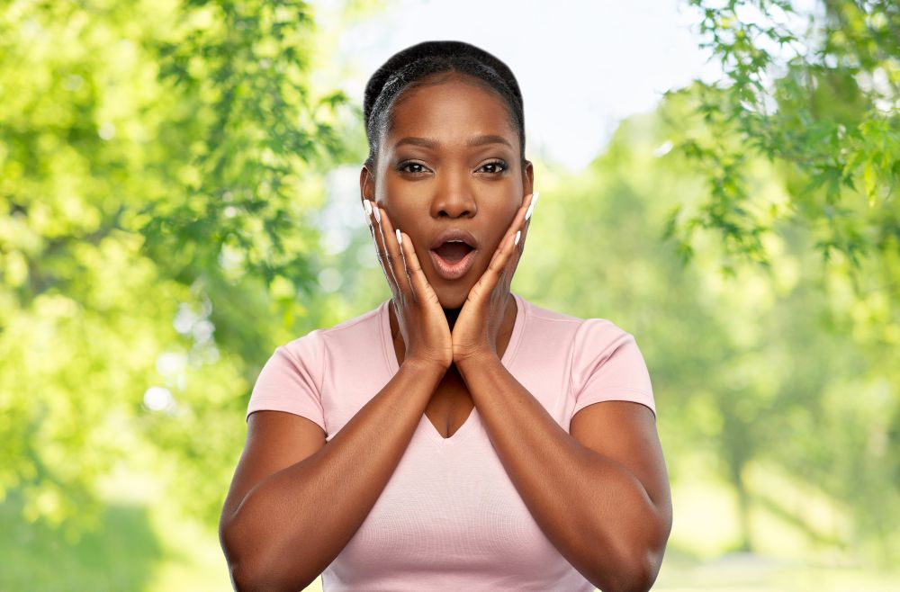 emotion, eco and people concept - shocked african american woman with open mouth over green natural background. shocked african american woman with open mouth