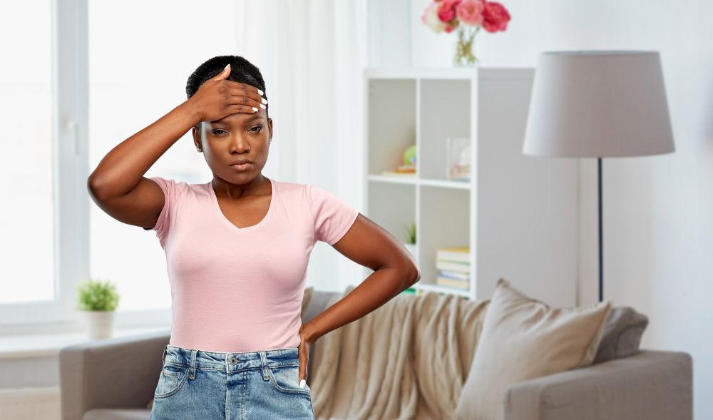 people, health problem and stress concept - unhappy african american woman suffering from headache or fever over home room background. african american woman having headache or fever