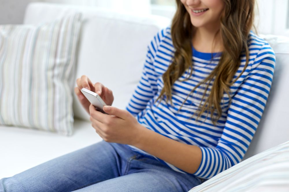 technology and people concept - close up of smiling teenage girl using smartphone at home. smiling teenage girl using smartphone at home
