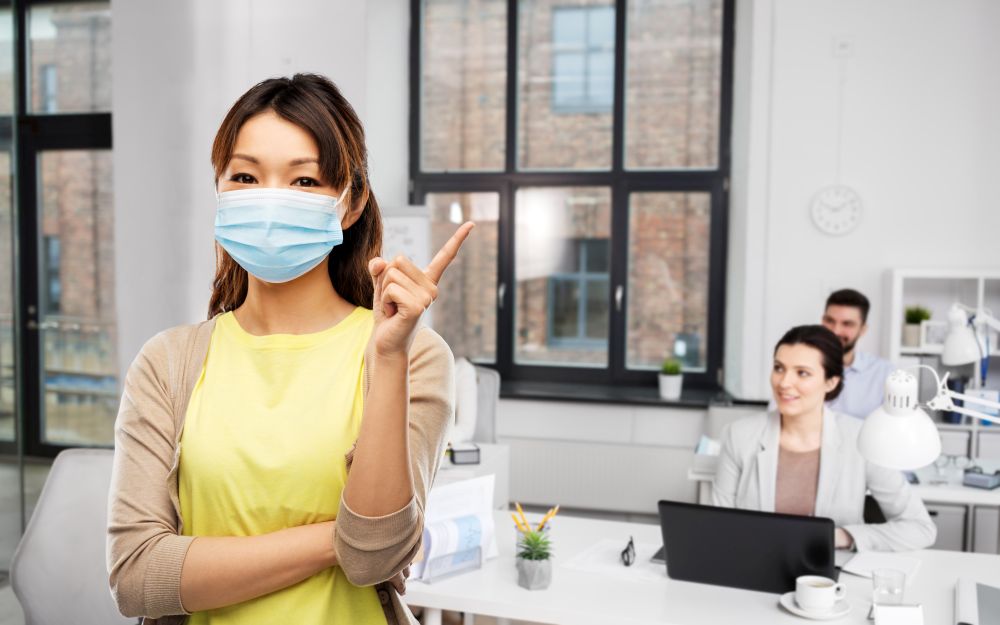 health, safety and pandemic concept - asian young woman wearing protective medical mask for protection from virus disease over office background. asian woman in protective medical mask at office