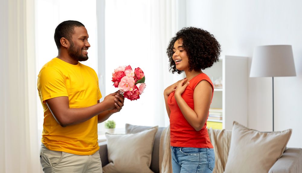 holiday, greeting and people concept - happy african american couple with bunch of flowers over home background. happy african american couple with flowers