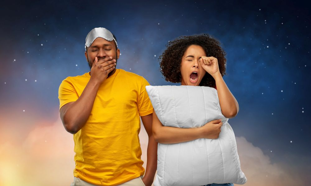 bedtime and people concept - african american couple with eye sleeping mask and pillow yawning over night sky background. african couple with eye sleeping mask and pillow