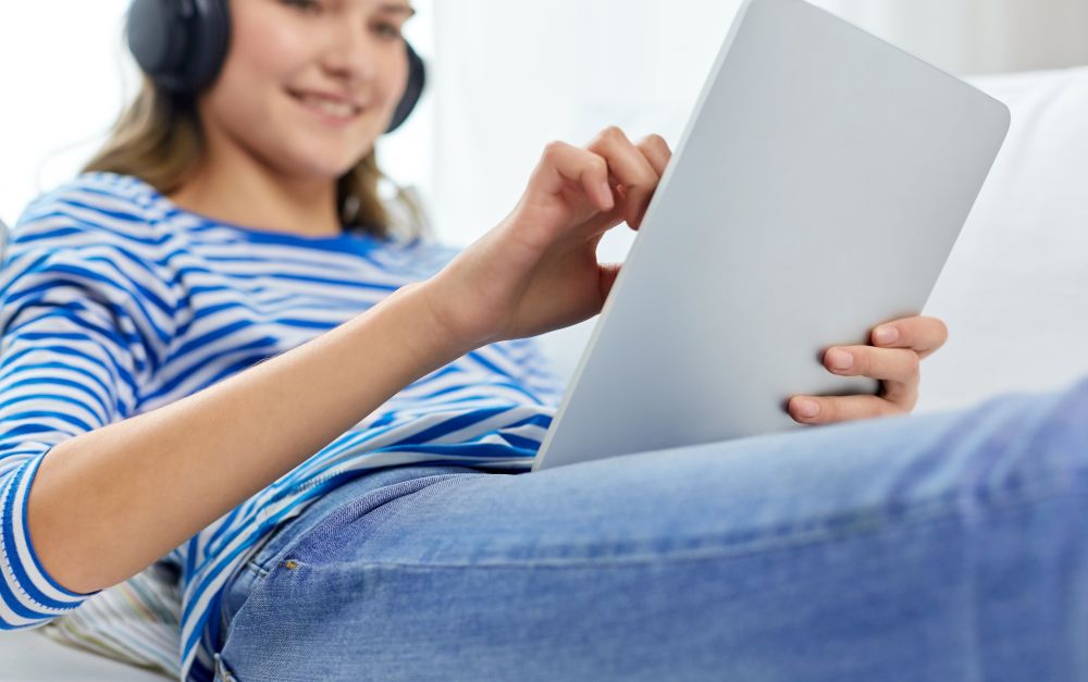technology and people concept - close up of happy smiling teenage girl in headphones listening to music on tablet pc computer at home. teenage girl listening to music on tablet computer