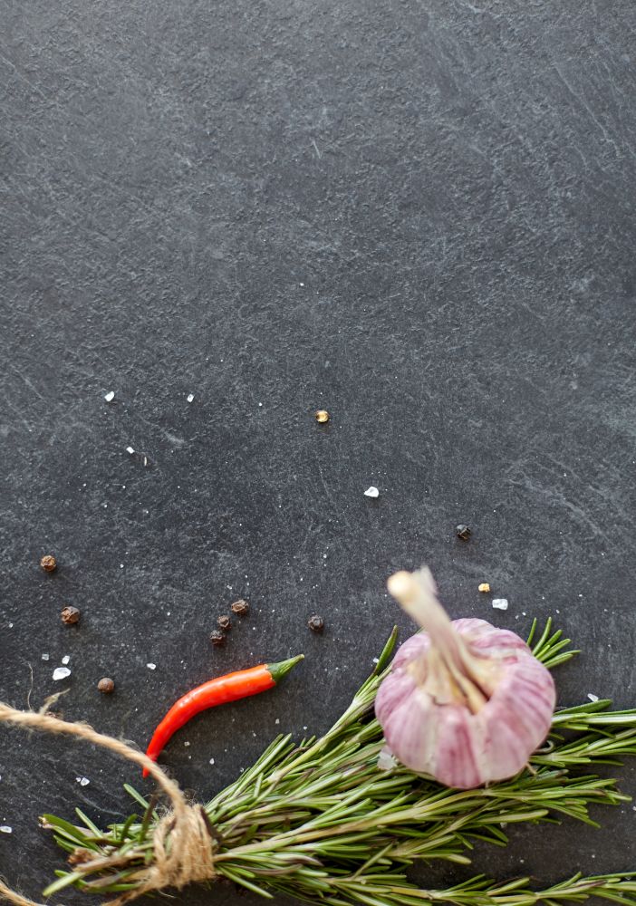 food, culinary and eating concept - rosemary, garlic, thyme and red chili pepper on stone surface. rosemary, garlic and chili pepper on stone surface