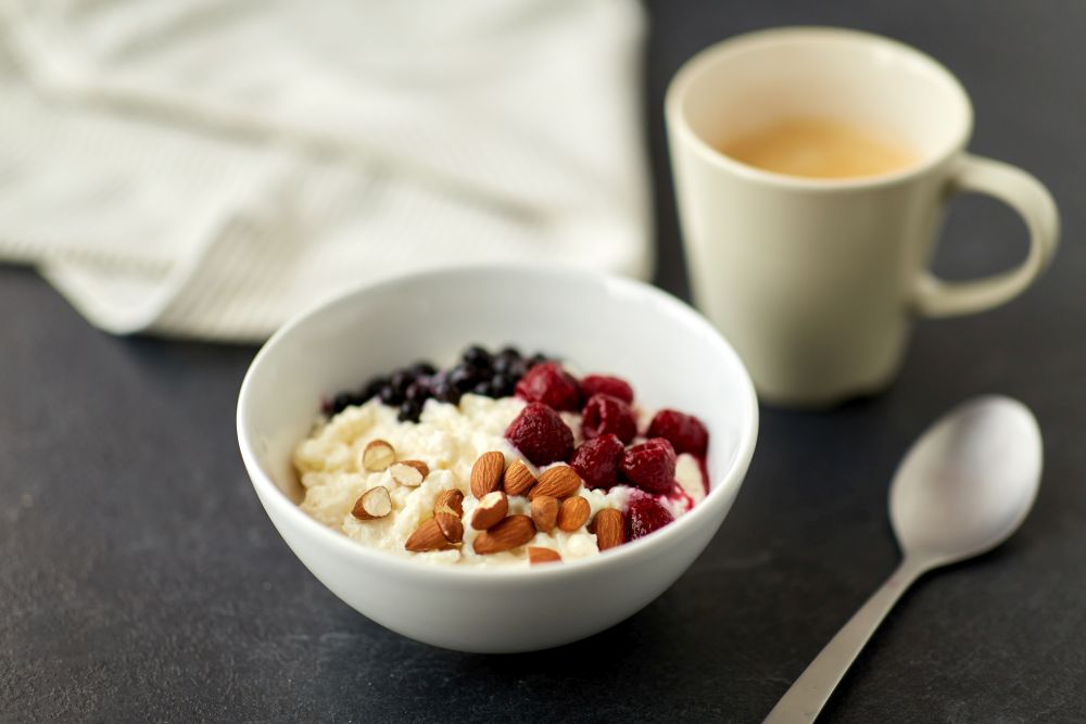 food and breakfast concept - porridge in bowl with wild berries, almond nuts, spoon and cup of coffee on slate stone table. porridge breakfast with berries, almonds and spoon