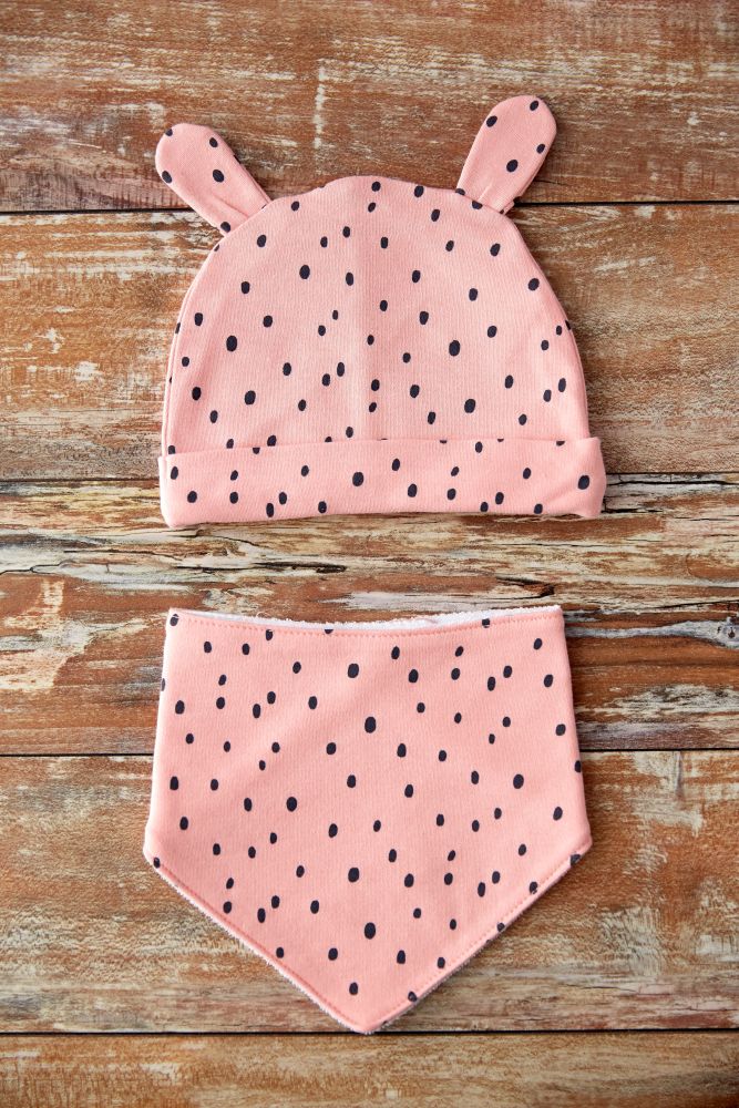 babyhood and clothing concept - pink baby hat with ears and bib with dot print on wooden table. pink baby hat with ears and bib on wooden table