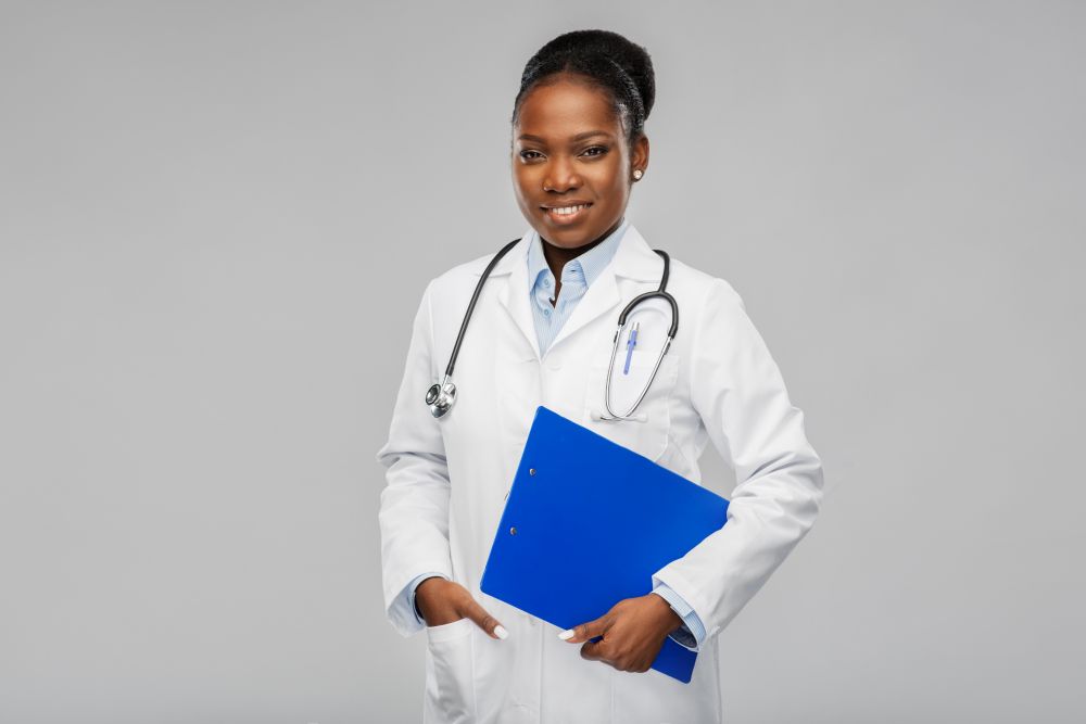medicine, profession and healthcare concept - smiling african american female doctor in white coat with clipboard and stethoscope over grey background. happy african female doctor with clipboard