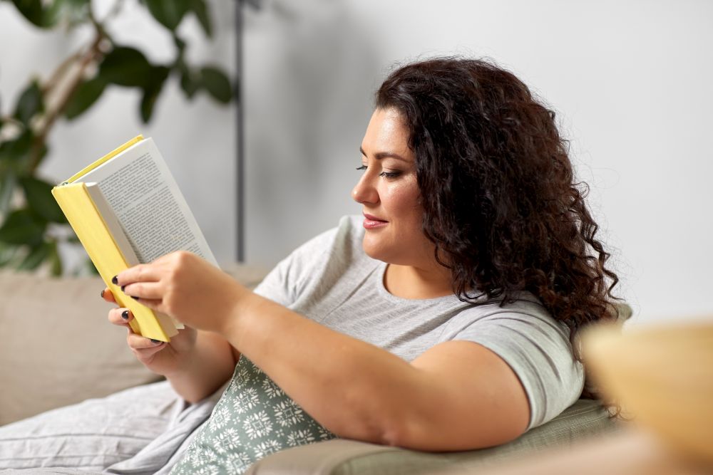 people and leisure concept - young woman reading book on sofa at home. young woman reading book on sofa at home