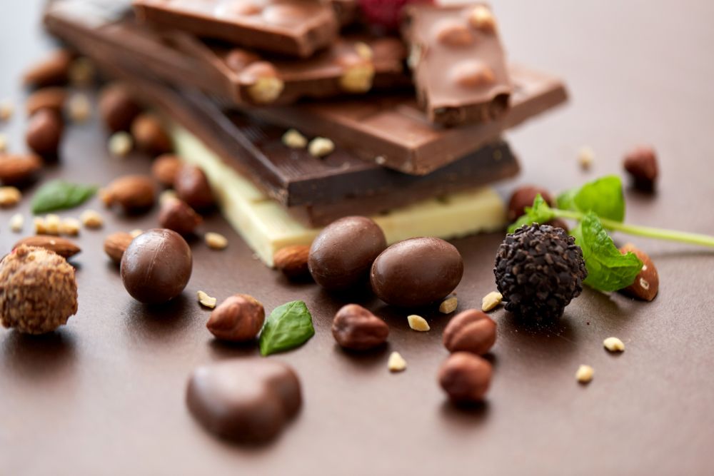 sweets, confectionery and food concept - close up of different chocolate bars, candies and nuts on brown background. close up of different chocolates, candies and nuts
