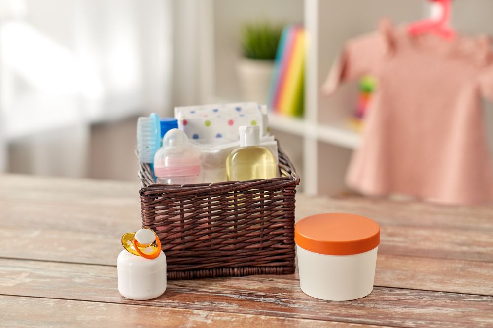 babyhood and care products concept - baby things in wicker basket on wooden table at home. baby things in basket on wooden table at home