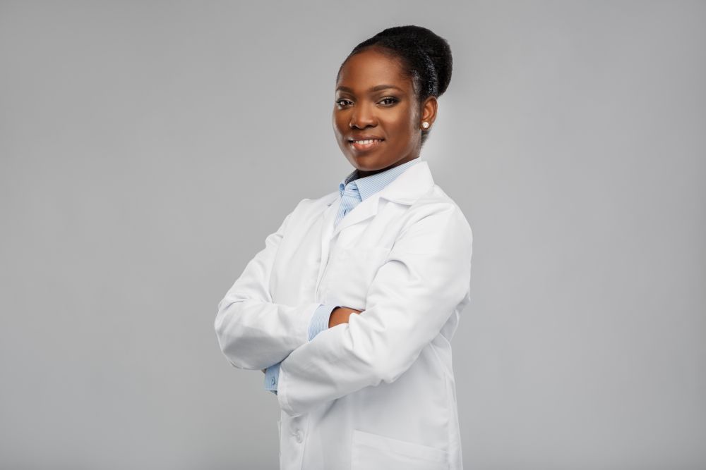 medicine, profession and healthcare concept - smiling african american female doctor or scientist in white coat with crossed hands over grey background. happy african american female doctor or scientist