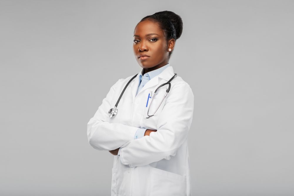 medicine, profession and healthcare concept - african american female doctor in white coat with crossed hands and stethoscope over background. african american female doctor with stethoscope