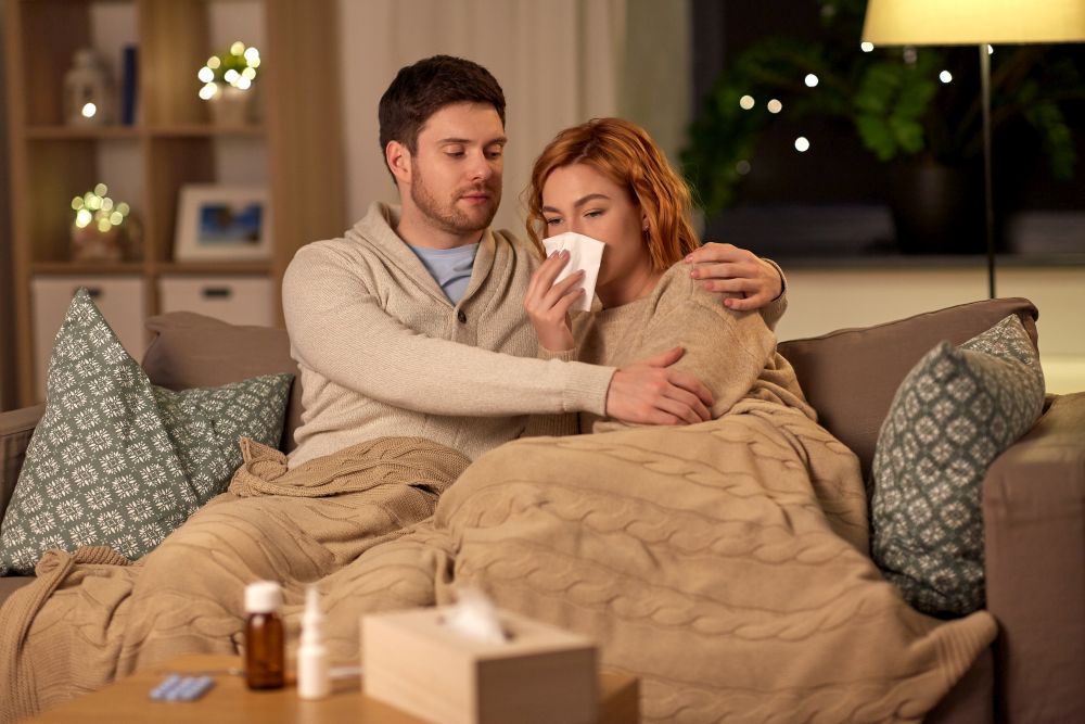 health, flu and people concept - sick young couple with tissue blowing nose at home. sick young couple with tissue blowing nose at home